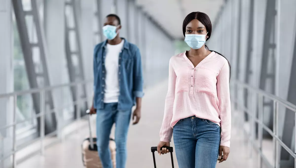 Couple at airport carrying luggage and wearing mask